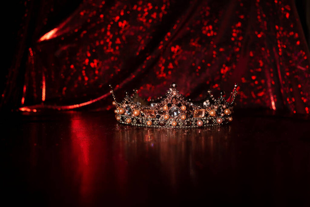 Koninklijke kroon met edelstenen op rode luxe stof achtergrond - Foto, afbeelding