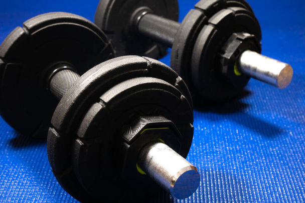 Heavy black dumbbells lying on the sports mat in the gym. Fitness sport motivation. Happy healthy lifestyle living. Exercises with bars weights. Home sport training. - Photo, Image
