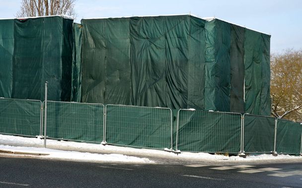 a group of workers covered the entire scaffolding, including the building, in green shading fabric. they are thus better protected from the wind. portable fencing in rubber weights around the building - Photo, Image