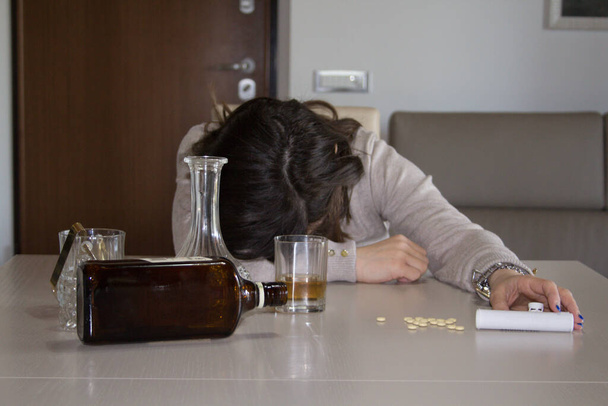 Изображение молодой женщины, потерявшей сознание на столе после злоупотребления алкоголем и психотропными препаратами. Ссылка на злоупотребление и зависимость этих веществ. - Фото, изображение