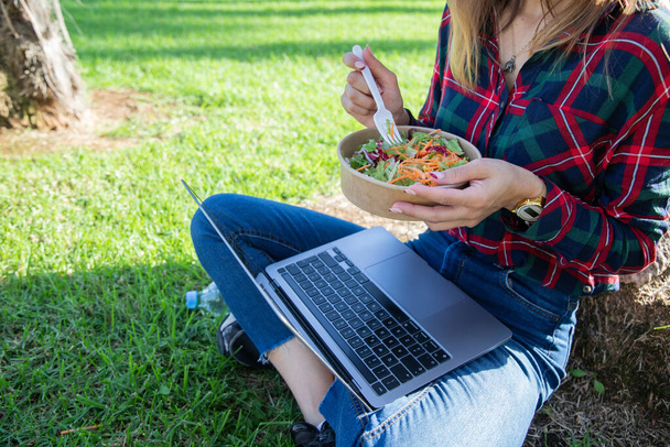 Zbliżenie sałatki, którą dziewczyna jada podczas przerwy obiadowej podczas pracy z laptopem - Zdjęcie, obraz