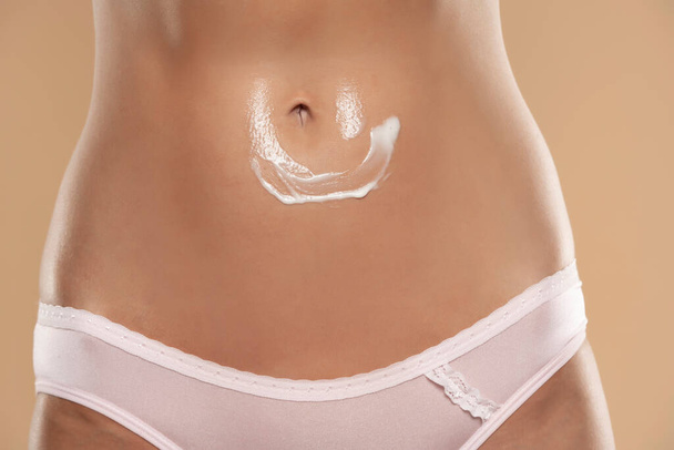 Close-up partial view of woman with body cream on belly on a beige studio background - Foto, Imagen