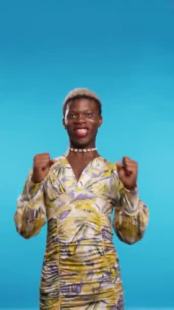 Modelo afro-americano animado em vestido elegante apertando punhos e gritando com os olhos fechados após a vitória contra o fundo azul. Vertical - Filmagem, Vídeo