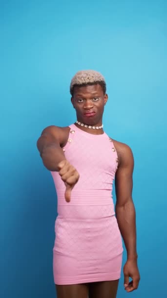 Walgelijke Afro-Amerikaanse man in stijlvolle jurk gebaren duim naar beneden en kijken naar camera tegen een blauwe achtergrond - Video