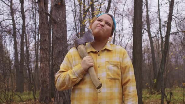 Ein Holzfäller kratzt sich im herbstlichen Wald mit einer Axt an seinem roten Bart. Porträt - Filmmaterial, Video
