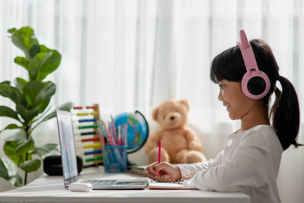 Asiatische kleine Mädchen mit Kopfhörern haben Videoanruf entfernte Klasse mit Lehrer mit Laptop, Online-Lernen am Computer, Homeschooling-Konzept - Foto, Bild