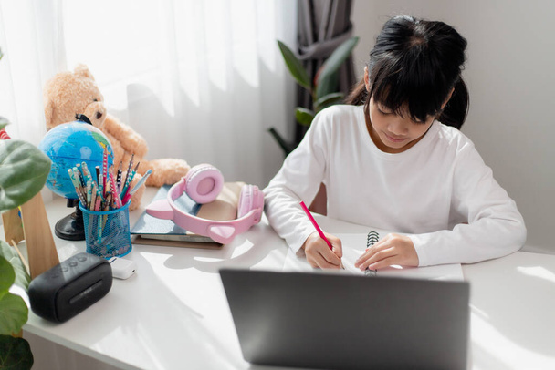 Aziatisch schoolmeisje doet haar huiswerk met laptop thuis. Kinderen gebruiken gadgets om te studeren. Onderwijs en afstandsonderwijs voor kinderen. Thuisonderwijs tijdens de quarantaine. Blijf thuis. - Foto, afbeelding