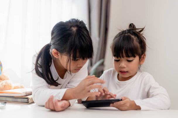 Çocukları ve aletleri kavrayın. İki küçük kız kardeş telefona bakar ve gülümser. Akıllı telefon videoları var, öğreniyorlar, oyunlar oynuyorlar, internette konuşuyorlar. Çocuklar için internet. Ebeveyn kontrolü - Fotoğraf, Görsel