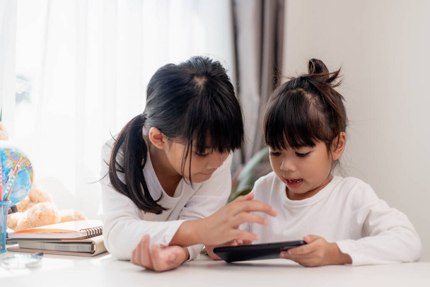 Koncepcja dzieci i gadżety. Dwie dziewczynki rodzeństwo Siostry patrzą na telefon i uśmiechają się. Trzymają filmy ze smartfonami, uczą się, grają w gry, mówią online. Internet dla dzieci. Kontrola rodzicielska - Zdjęcie, obraz