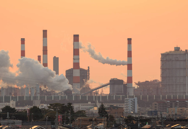 Il fumo sorge dall'impianto industriale con arancio bagliore del tramonto nel cielo. Foto di alta qualità - Foto, immagini