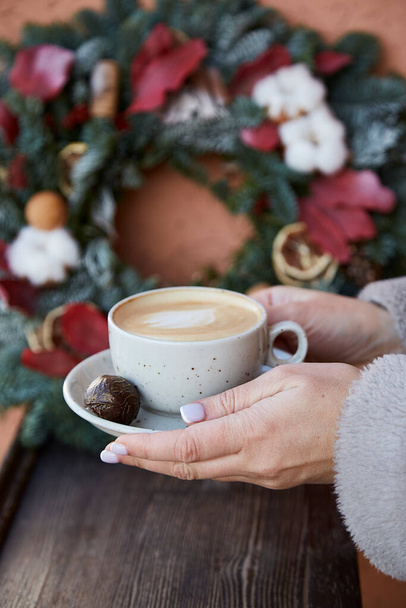 Kadın elleri dışarıda şık bir Noel çelengi önünde bir fincan kahve tutuyor. Konforlu bir festival evi. Yeni yıl sabahı. - Fotoğraf, Görsel