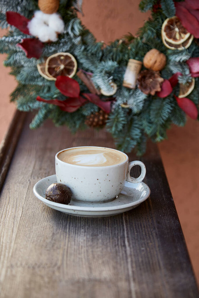 Elegant Christmas wreath and cup of coffee at the terrace. Cozy festive home. New Year morning. - Photo, Image