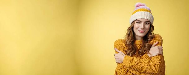 Atrakcyjny kobiecy delikatny młoda kobieta czuje się przytulnie, obejmując się uśmiechnięty zachwycony słodkie, nosząc komfortowy ciepły sweter modny kapelusz przytulanie, śniący chłopak przytula, stać żółte tło. - Zdjęcie, obraz