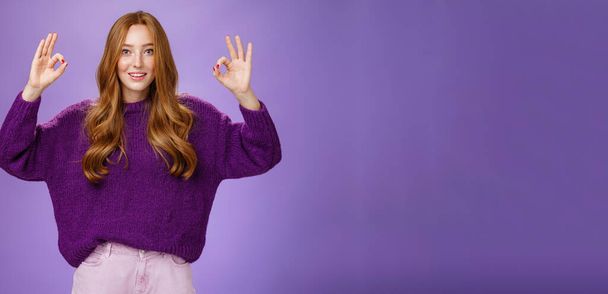 Bien, estoy de acuerdo. Retrato de amigable y optimista joven veinteañera jengibre en suéter púrpura levantando las manos con el gesto bien o bien sonriendo en aprobación, gustando producto fresco, dando recomendación. - Foto, Imagen