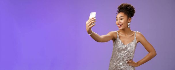 Pewny siebie zadowolony atrakcyjne stylowe millenium afrykańsko-amerykański. kobieta w srebrnym błyszczące sukienka biorąc selfie pozowanie słodkie sassy trzymać rękę talia przedłużyć ramię rekord wideo wiadomość podczas nocy-out. - Zdjęcie, obraz