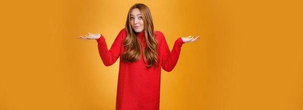 What do I know. Portrait of confused clueless tender and gentle redhead woman in red sweater shrugging with hands raised near shoulders turning away questioned and unaware, not knowing. - Photo, Image
