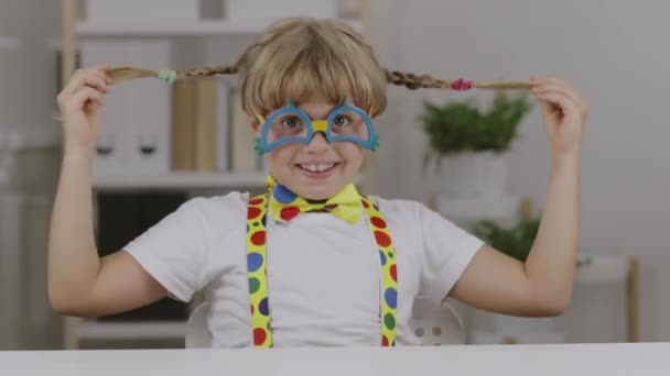 Funny girl de 7 ans vêtue de lunettes de clown, papillon et bretelles. Images 4k de haute qualité - Séquence, vidéo