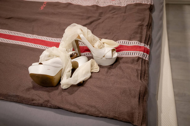 Άσπρα ψηλά τακούνια και ψηλά κάλτσες ξαπλωμένες σε μια κουβέρτα σε ένα κρεβάτι. - Φωτογραφία, εικόνα