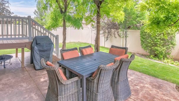 Panorama Outdoor patio with covered barbecue grill under a pergola roof with vines. There are woven chairs tucked into table near the wooden deck on the side and a view of a vinyl fence and lawn. - Photo, Image