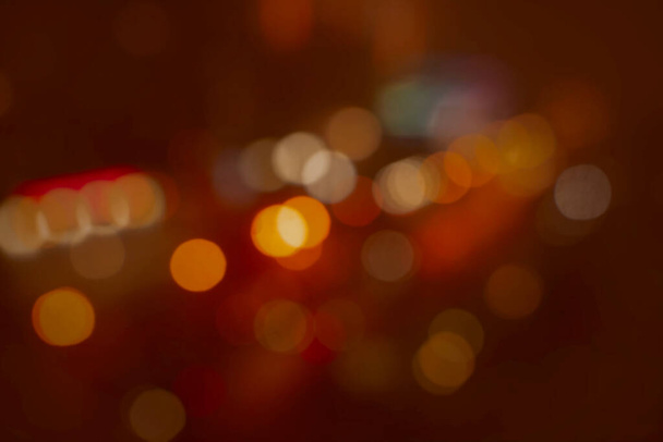θολή και αποσυντονισμένα φώτα της πόλης νύχτα - κόκκινο κίτρινο σε πορτοκαλί φόντο. εορταστική διάθεση φωτεινό φόντο αφαίρεσης στην επιφάνεια εργασίας - Φωτογραφία, εικόνα