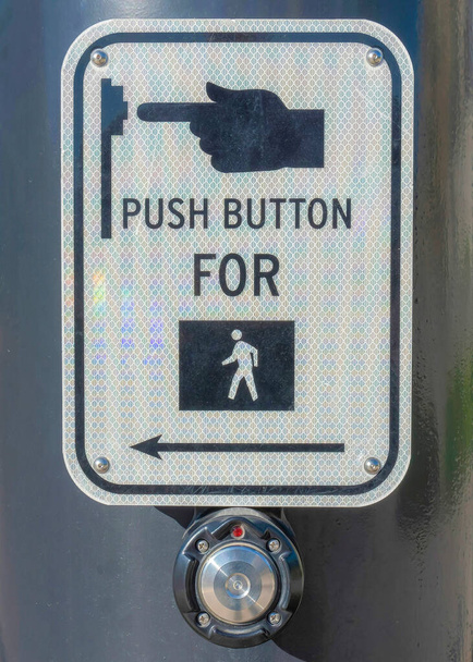 Pionowy przycisk dla pieszych na czarnym słupie w Daybreak w południowej Jordanii, Utah. Zamknij znak z naciśnięciem przycisku dla pieszych symbol przed widokiem na boczny spacer i drogi w pobliżu domów. - Zdjęcie, obraz