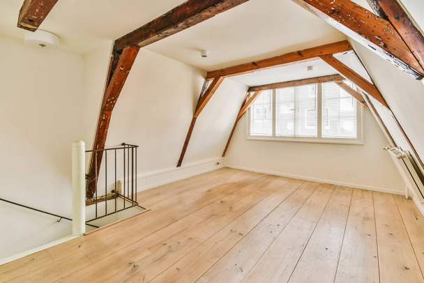 Кімната в горищному стилі з дерев'яною підлогою і відкритими балками на стелі в цьому будинку дуже добре мебльована
 - Фото, зображення