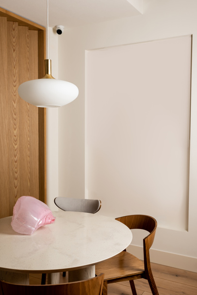 decorative pink figurine on round dining table near wooden chairs in hotel room with security camera  - Fotó, kép