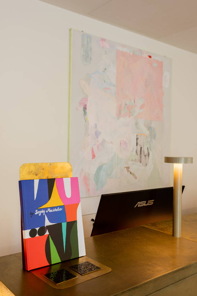 abstract painting on wall near reception desk with art book and computer monitor  - Photo, image
