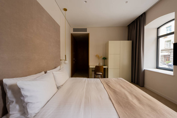 現代的なホテルのベッドルームで机と椅子の近くに白い寝具付きの快適なベッド - 写真・画像