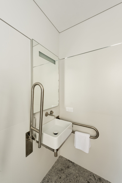 салон белой ванной комнаты с раковиной и зеркалом для инвалидов в отеле  - Фото, изображение