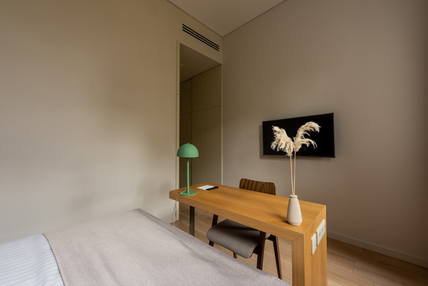 деревянный стол и телевизор с чистым экраном на стене рядом с кроватью в номере отеля  - Фото, изображение