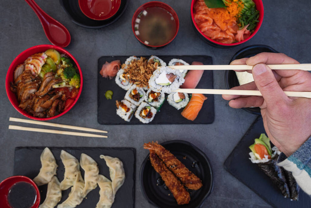 Veduta delle mani dell'uomo che mangia sushi nel ristorante giapponese. Vista ad alto angolo delle mani di sushi con bacchette sul tavolo - Foto, immagini