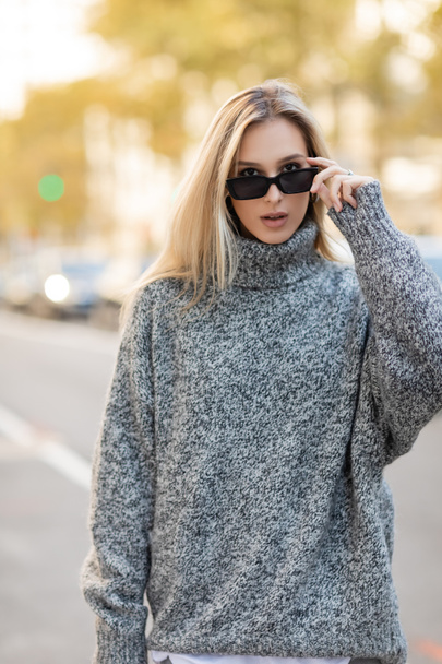 портрет блондинки в сером свитере, регулирующей модные солнцезащитные очки на улице Нью-Йорка  - Фото, изображение