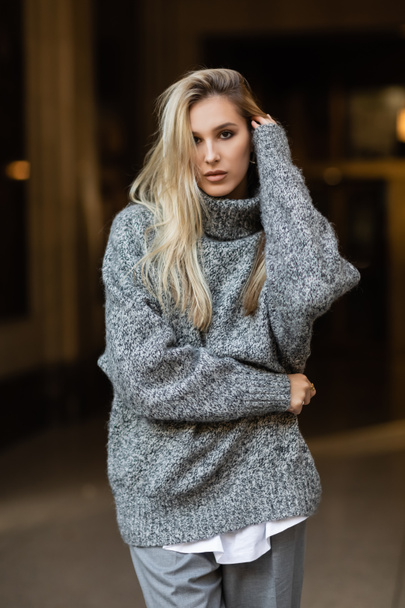young and blonde woman in grey outfit looking at camera while posing on street of New York in winter  - Foto, imagen