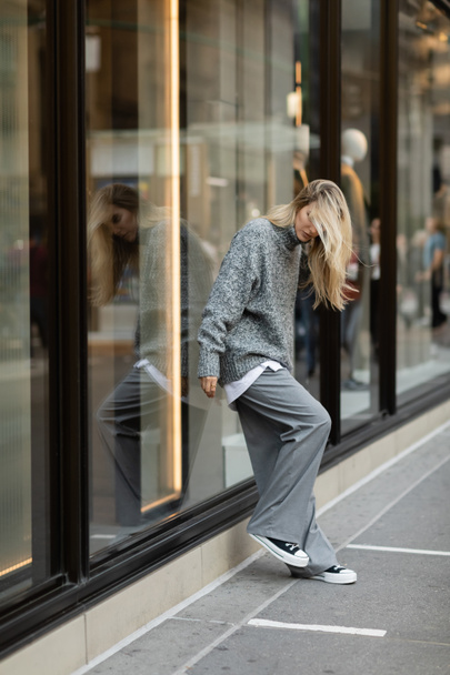 full length of young woman in stylish grey outfit standing near window display in New York  - Фото, зображення