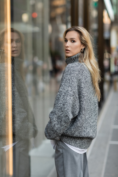 blonde woman in grey winter outfit standing near glass window display in New York  - Photo, Image