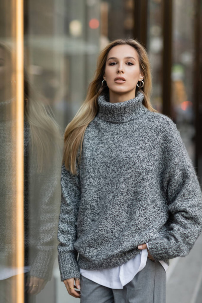 Молода жінка в зимовому одязі стоїть з рукою в кишені біля вікна показу в Нью - Йорку.  - Фото, зображення