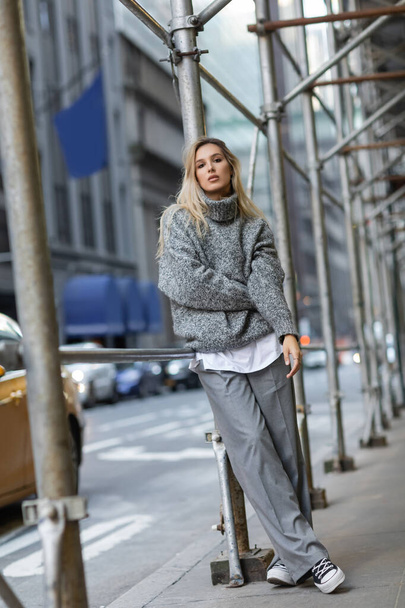 volledige lengte van jonge vrouw in grijze winter outfit leunend op straatpaal en auto 's in New York  - Foto, afbeelding