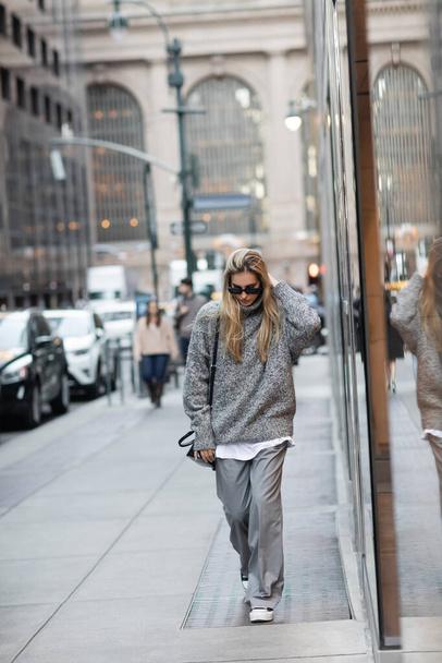 tutta la lunghezza della donna in maglione invernale e occhiali da sole a piedi con borsa sulla strada urbana di New York  - Foto, immagini
