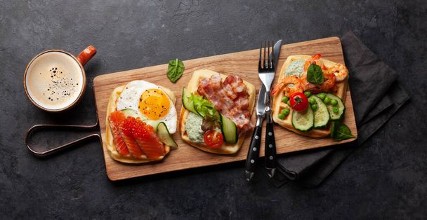 Desayuno gofres con huevos fritos, salmón, tocino, pepino y gambas. Vista superior plano con café - Foto, Imagen