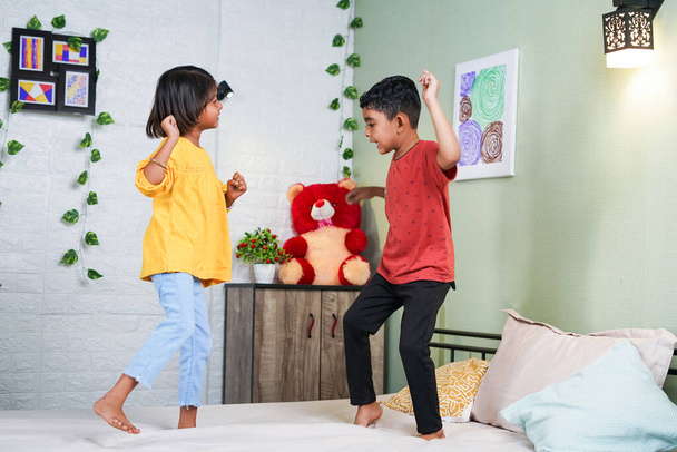 Счастливые улыбающиеся дети, танцующие, прыгая на кровати дома - концепция игривого детства, связей и отношений - Фото, изображение