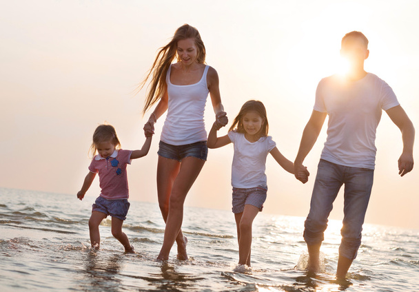 Happy young family having fun running on beach at sunset - Fotoğraf, Görsel