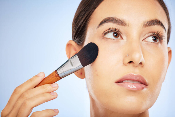Woman, face and thinking with makeup brush for skincare beauty, luxury skin wellness and cosmetics dermatology in studio. Facial care, product application or spa vision aesthetic in blue background. - Photo, image