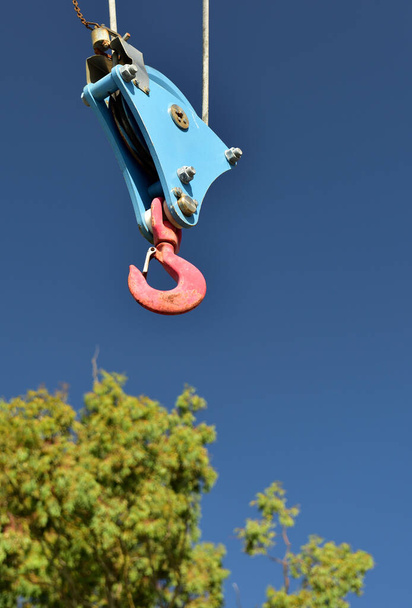 Un gancho de grúa de puerto resistente colgante anticipando una recogida con un árbol como fondo - Foto, imagen