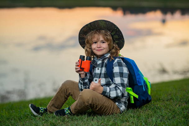 Feliz niño jugando con prismáticos. Explora y aventura. Niño con mochilas explorando la naturaleza y el medio ambiente. Actividad de ocio al aire libre para niños. Viaje de verano para turistas - Foto, imagen