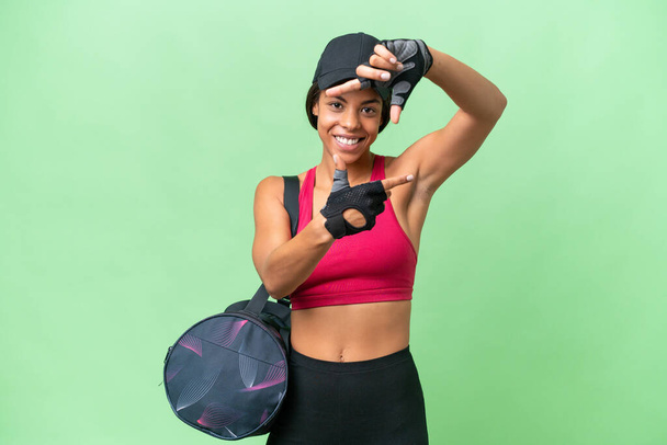 Junge Sport Afroamerikanerin mit Sporttasche über isoliertem Hintergrund fokussiert Gesicht. Framing-Symbol - Foto, Bild