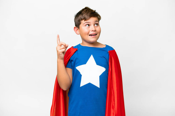 Super hrdina běloch dítě přes izolované bílé pozadí s úmyslem realizovat řešení a zároveň zvednout prst nahoru - Fotografie, Obrázek