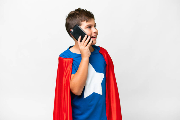 Хлопчик-супергерой через ізольований білий фон, тримаючи розмову з мобільним телефоном - Фото, зображення