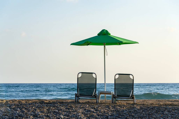 Plażowe leżaki pod zielonymi parasolami nad brzegiem morza, koncepcja wypoczynku i relaksu, wschód słońca, letni słoneczny dzień, błękitne niebo przestrzeń do kopiowania - Zdjęcie, obraz