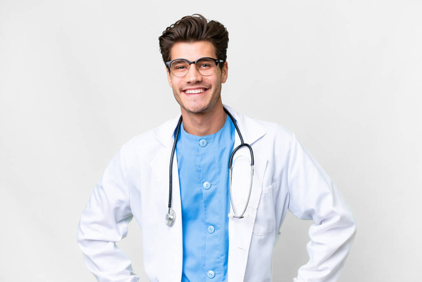 Young doctor man over isolated white background posing with arms at hip and smiling - Foto, Imagen